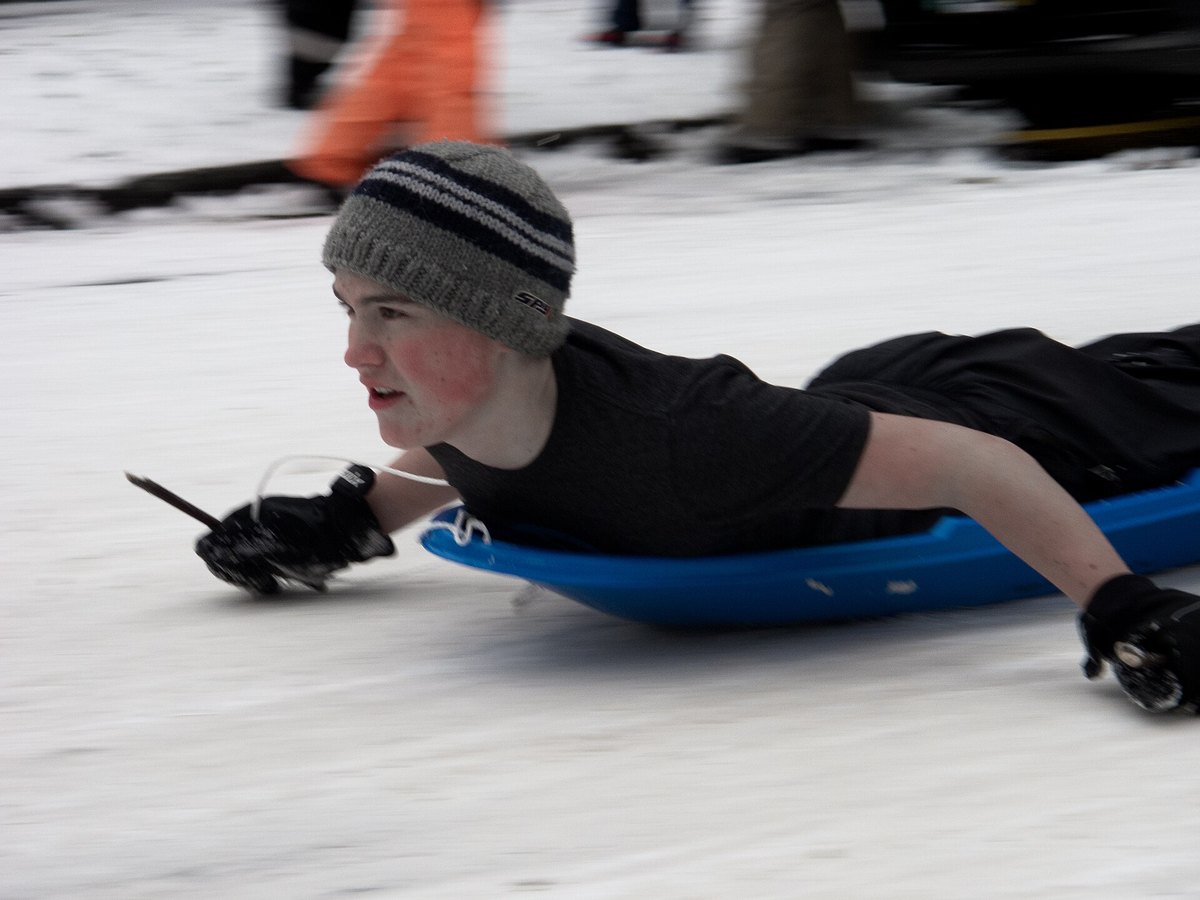 Junge rutscht schnell kopfüber auf einem Schlitten über eine Eisfläche