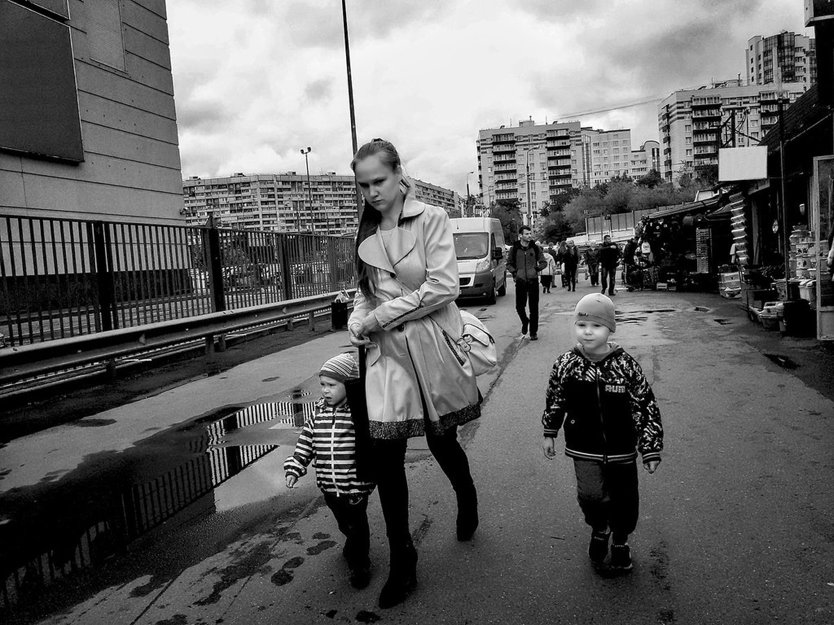 Mutter geht mit zwei kleinen Kindern durch eine Stadtstraße